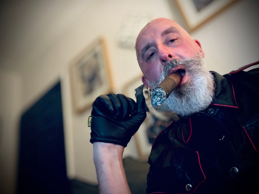 60 year old man with a white beard, wearing a black
leather shirt and black leather gloves, with a large cigar in his mouth.
