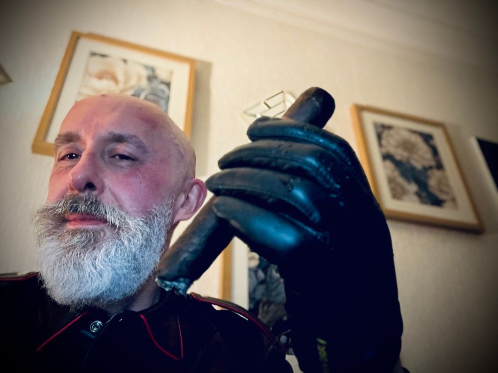 Smiling , white bearded man, bald headed and holding a large cigar in a black leather gloved hand 