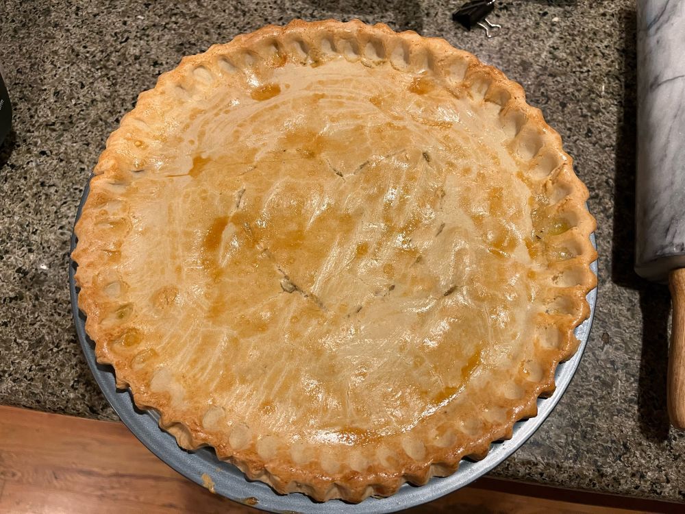 A round pie with perfect, golden crust. In the middle, a simple heart is carved into the crust to vent steam. 

A marble rolling pin with a wooden handle is partially visible to the right of the pie plate. 
