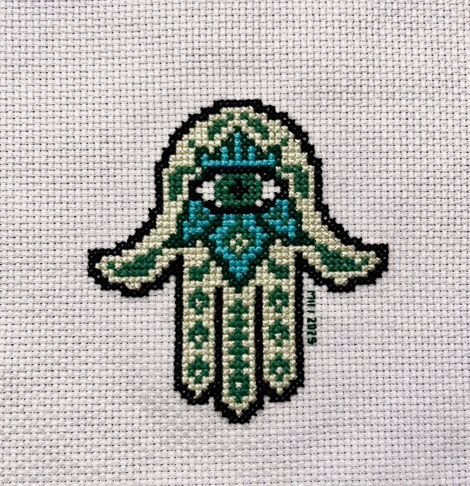 Cross stitched hamsa with the fingers pointing down. Decorative elements are vaguely plant-like. 