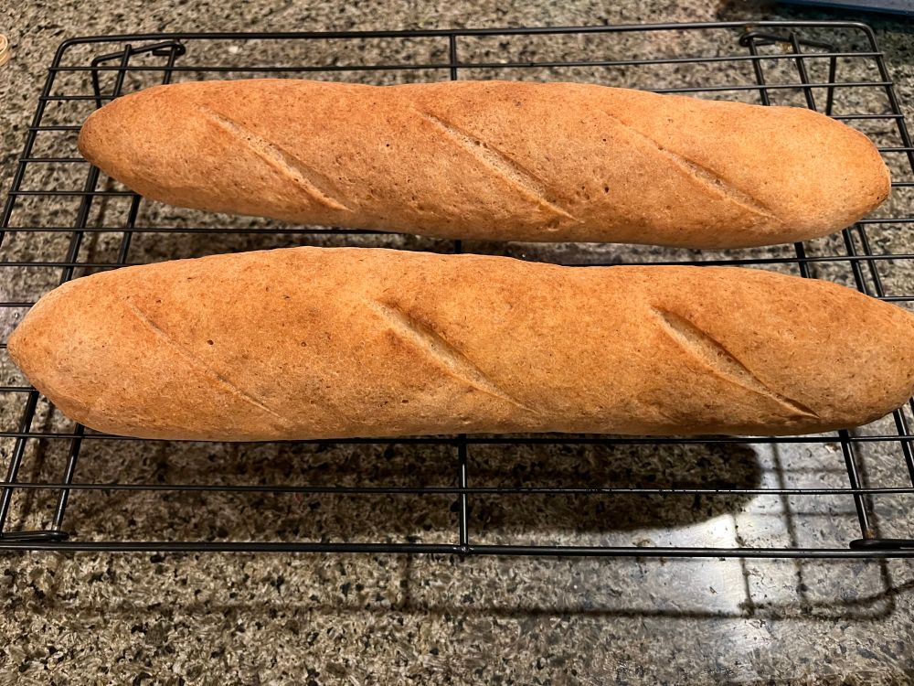 Two golden brown baguettes on a cooling rack. 