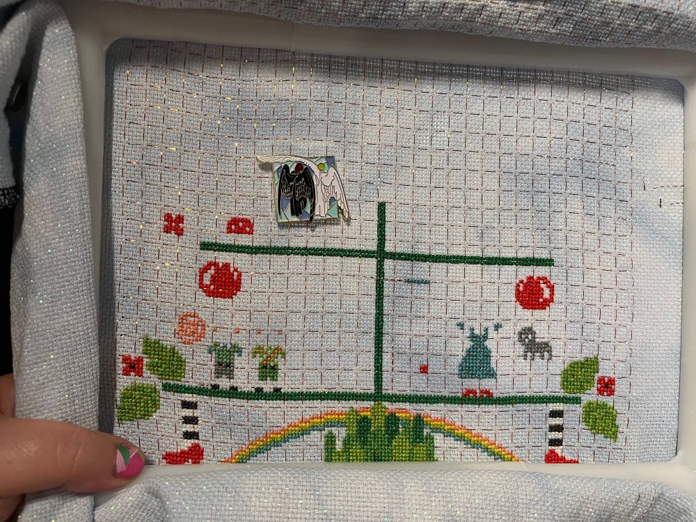 102 stitches tonight

In-progress capture of The Wizard of Oz Tree by tiny modernist cross stitch. Tucked into the bottom of the Q-snap, you can see a rainbow over the towers of the Emerald City. On either side of the rainbow, striped sticking with red shoes hang down from a tree branch. Each side of the branch also sports some leaves and a red flower. And there are some red blobs. And some colorful clothing. 

The Needle minder shows the backs of two angels, one with black wings and one with white. Three of the wings hang loosely behind them.  One of the white wings is lifted above the head of the angel with black wings, as if to guard him from falling rain. 