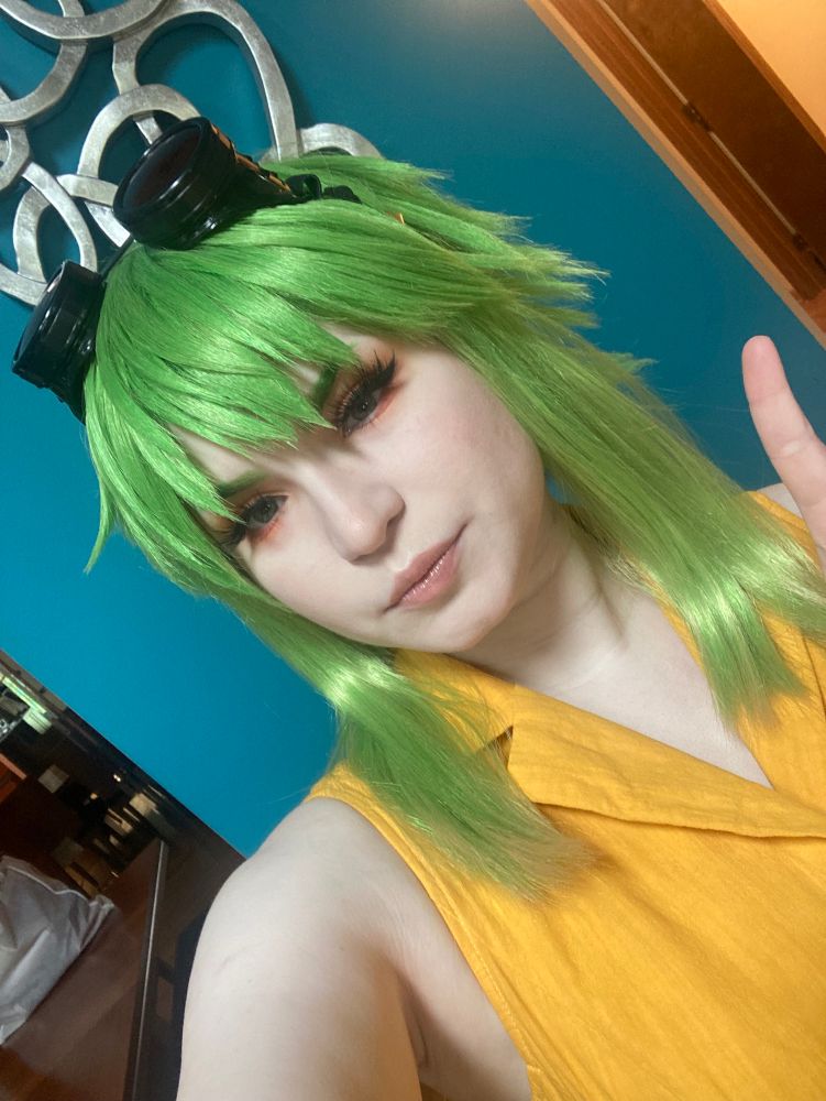 Cosplay selfie of Gumi Megpoid in her outfit from Ten-Faced against a blue wall