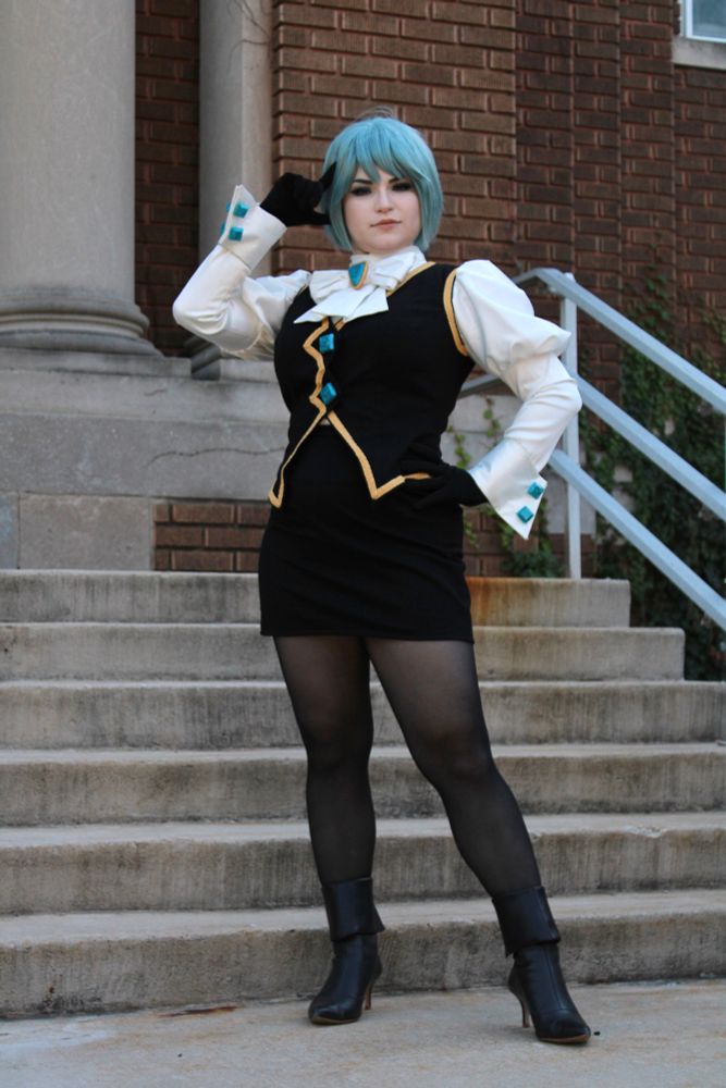 Cosplay of Franziska von Karma from Ace Attorney, standing in front of stairs. One hand is on her hip and the other is pointed near her head.