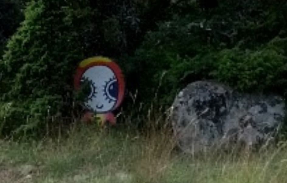 Screenshot of a cropped 360 photo focusing on a cartoonish figure peering out from behind a bush.