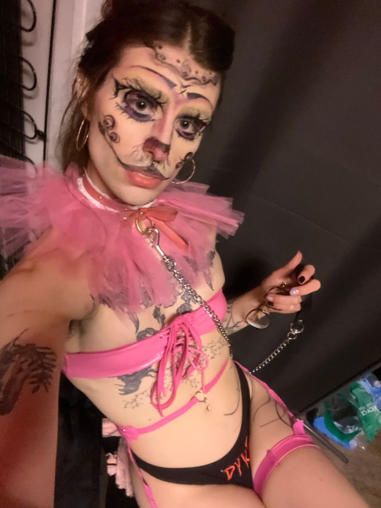 woobie sitting backstage, you looking down at her. she's in a pink frill, pink and white collar with chain leash, pink garters and pink bra band, and black panties with the work DYKE on the crotch in red. she's in bunny clown make up and she's looking up at you like....what you don't like the panties on?