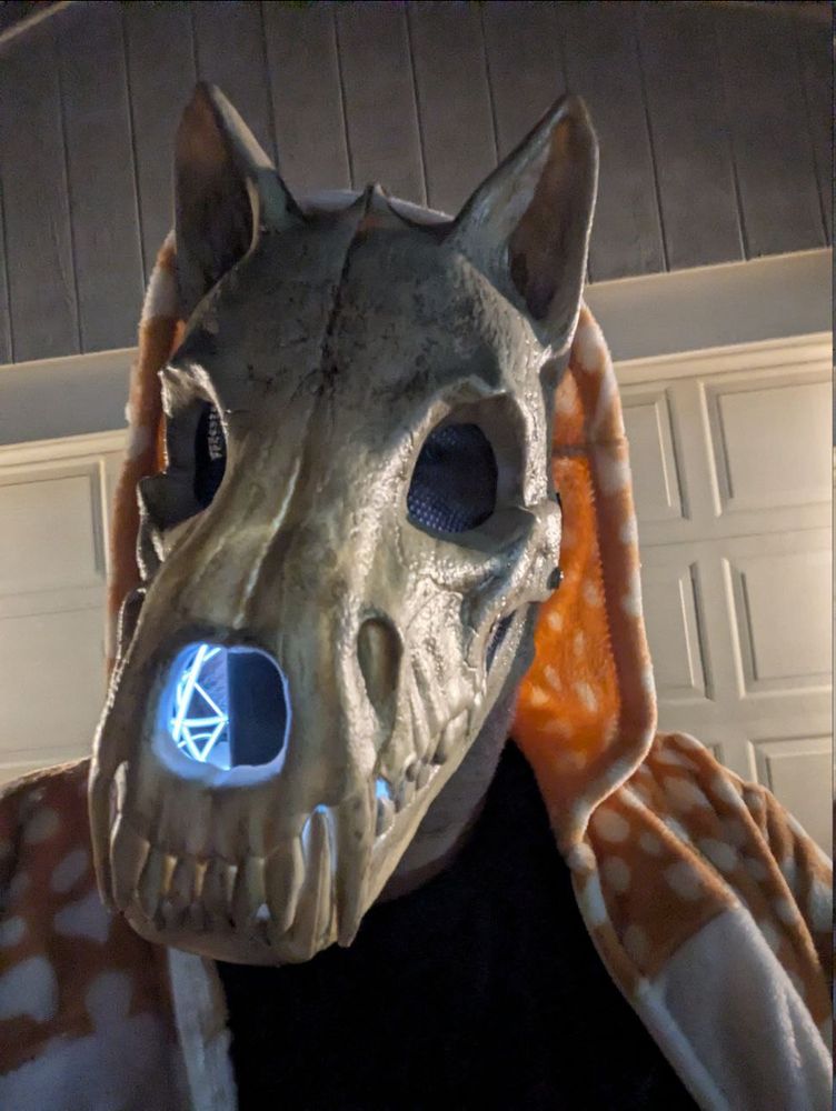 A goofball wearing a deer kigu and a werewolf-skull mask that seems to have some white lights inside the muzzle.