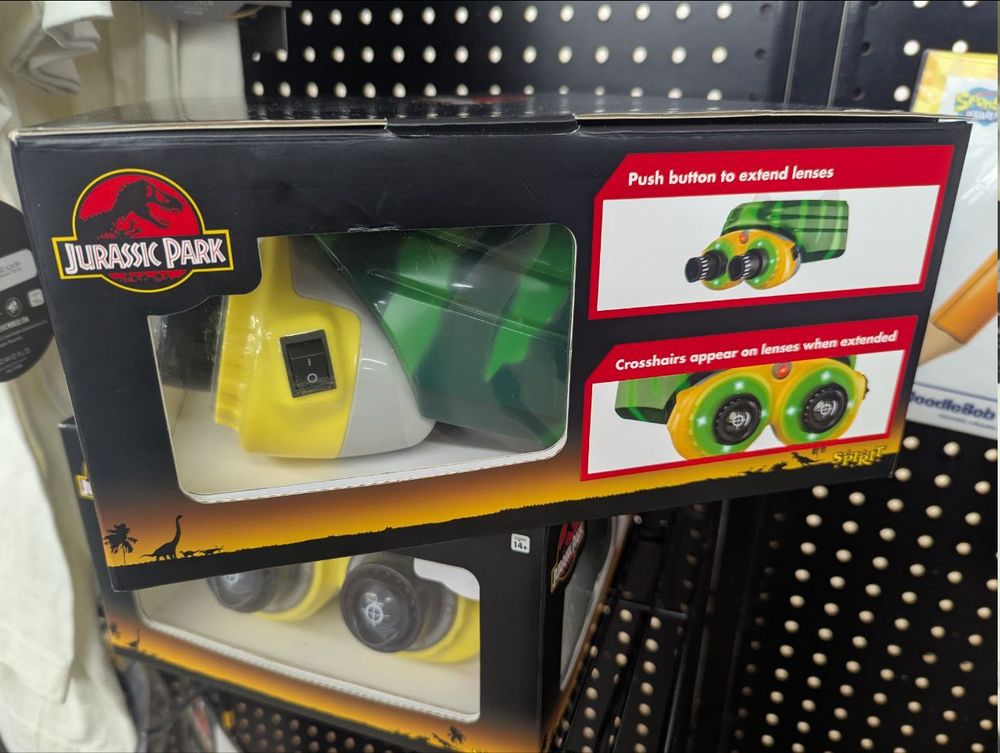 A photo of some black and yellow goggles, a replica of a prop from Jurassic Park. The lenses have crosshairs painted on them. The box instructs you to push button to extend lenses, and mentions crosshairs appear on lenses when extended.