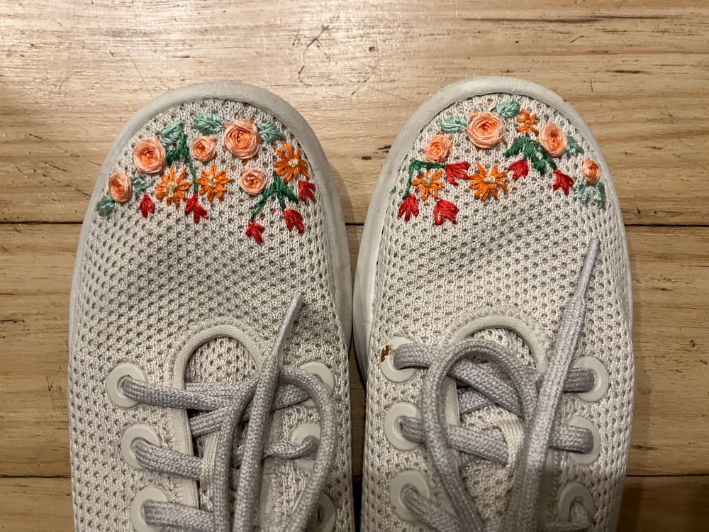Close up of sneakers with flowers embroidered on the toes.