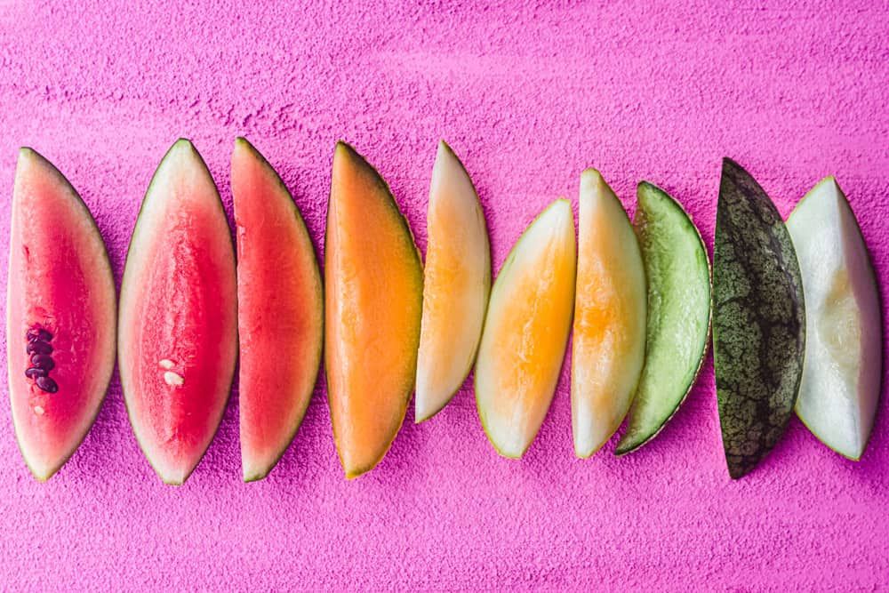 Photo of slices of various types of melons, arranged in a color spectrum from red through green.