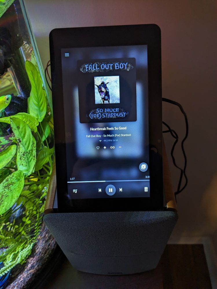 A display showing Fall Out Boy on Volumio, sitting on a powered bookshelf speaker with an aquarium next to it. 
