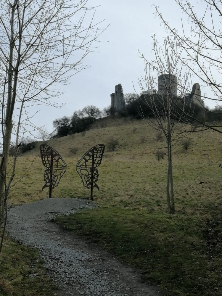 Eine Burgruine, einige Meter davor ein Tor in Schmetterlingsform.