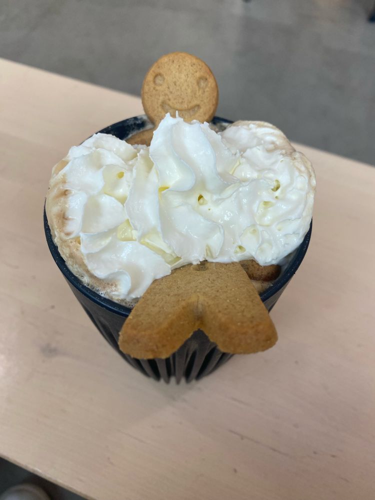 Very happy looking gingerbread man sat in a bubble bath of whipped cream (on top of a coffee)