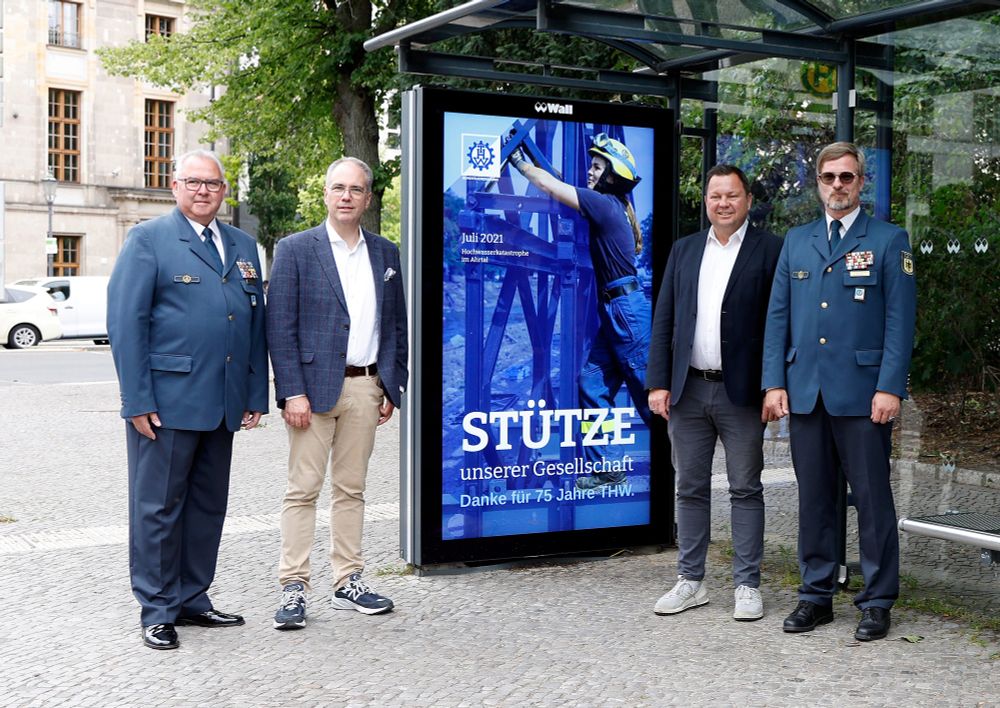 Markus Jaugitz, Vizepräsident THW-Bundesvereinigung, Patrick Möller, Geschäftsführer Städtemarketing & Service Wall, Martin Gerster MdB, Präsident THW-Bundesvereinigung und Christian Herrmann, Vizepräsident THW-Bundesvereinigung, vor dem Plakat mit dem Text "Stütze unserer Gesellschaft. Danke für 75 Jahre HTW.