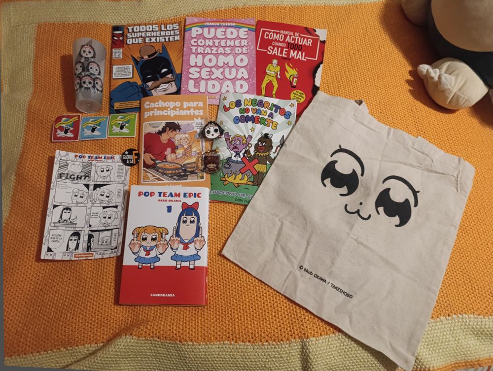 Fotografía en la que muestro diversas cosas que compré en el salón manga Barcelona: un vaso alargado de plástico con la mascota Onachan dibujado en el dibujo se aprecia que hay varias haciendo una pirámide subiéndose una encima de otra , un fanzine llamado cachopo para principiantes, un cómic llamado todos los superhéroes que existen, otro llamado puede contener trazas de homosexualidad ,otro que se llama manual de como actuar cuando todo sale mal , tres pegatinas de Kumamon ( de colores magenta , celeste y verde pistacho) un cómic hecho como si fuera un cuaderno de actividades que se llama los negritos no van a comerte , el manga de pop team epic, unas pegatinas del susodicho manga de varias viñetas ( en la primera se ve a Popuko en modo pelea y un fight debajo , en la segunda dice espero que gracias a esto muera muchisima gente pero con que solo muera una persona ya habrá valido la pena , en la tercera escribe un poema que dice cierra la boca , cierra la puta boca , cierra la boca , en la cuarta aparece con dos telefonos en ambos oídos y dice a uno hola ¿Policía? Fandogamia ha vuelto a hacerlo , en la quinta Pipimi está subida con muchos micrófonos y hace un corte de manga con la mano derecha , en la sexta Popuko señala con la mano derecha diciendo ah...you are motherfucker? , en la séptima Pipimi dice no estás bien de la cabeza y en la octava ambas lloran porque han arrestado a Popuko por ser youtuber y hay un panel que lo dice "arrestada por youtuber" y por último hay una totebag con la cara "pop team epic" ya que ambas tienen la misma cara ( ojos grandes animescos , un puntito simulando una nariz y una boca de gatito) y en la parte derecha se ve parte de un peluche de snorlax.