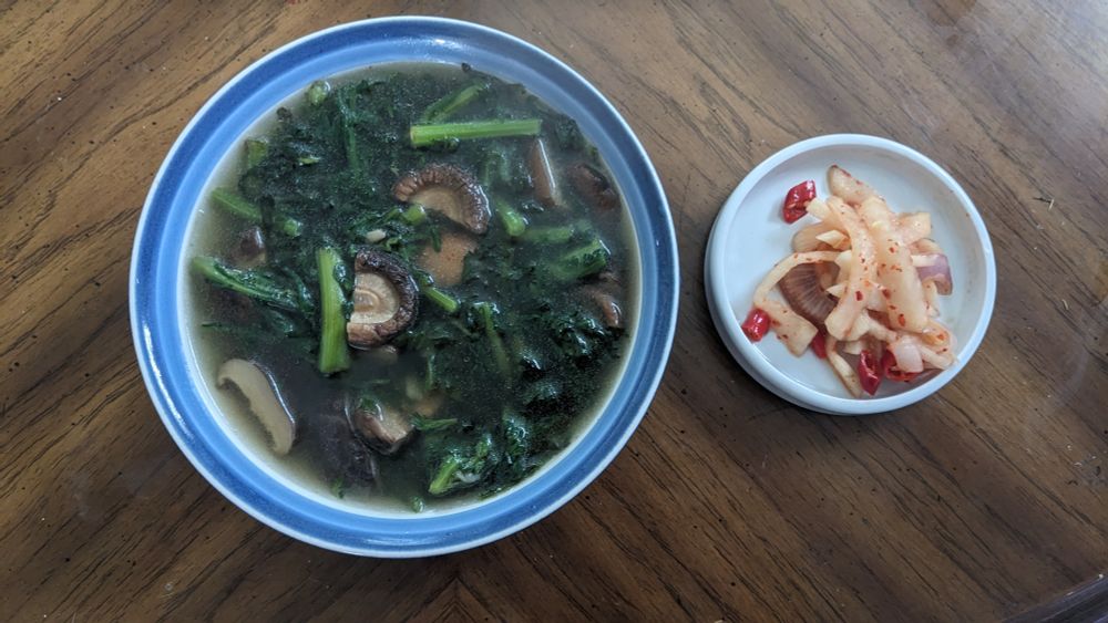 a bowl of soup next to a small ceramic dish of red tinted daikon with chilis and shallots