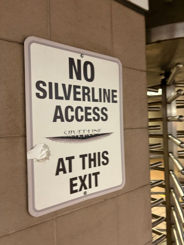 Sign on wall near turnstile. Sign says “No silver line access at this exit” and has the silver line logo in the middle of the sign.