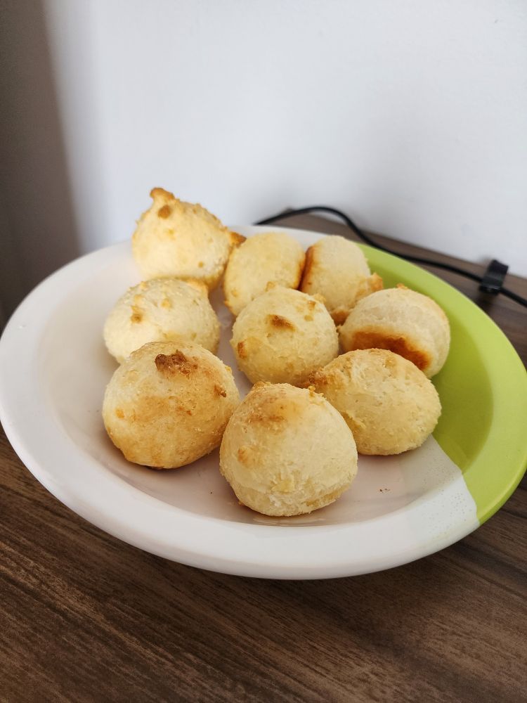 Prato com pães de queijo assados em uma mesa de madeira