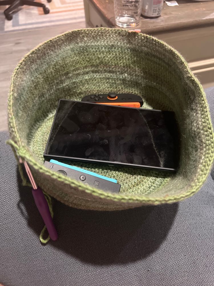 A green crochet bag in progress with a Switch 2 in it for scale