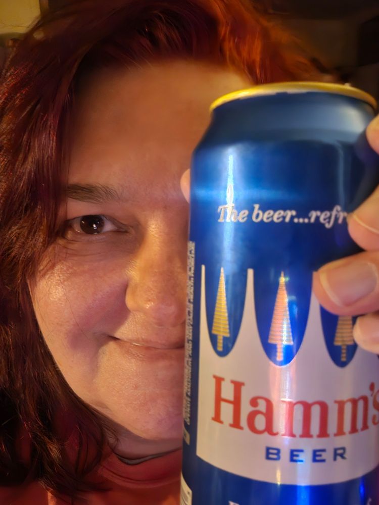 My nearly 60yr old self with red hair (for now), sort of smiling and covering half of my face with a can of Hamm's beer because that's a cool way to take a selfie, right?