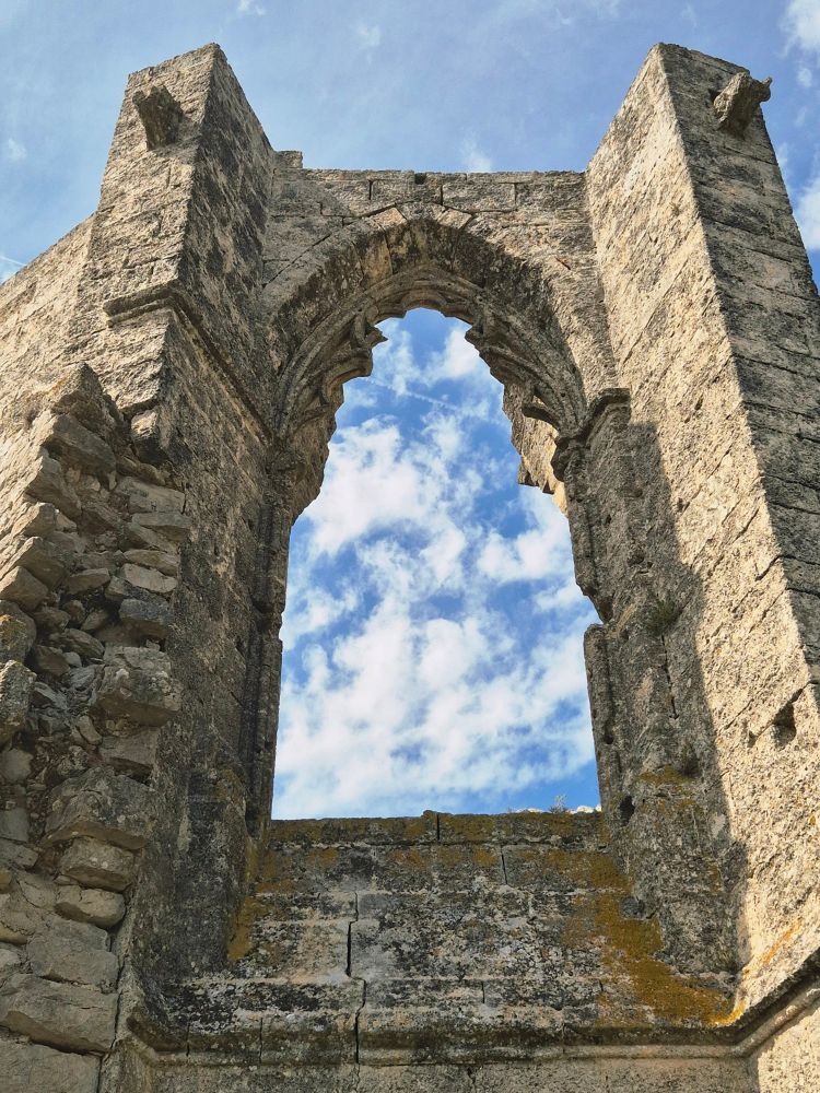 Blick durch ein großes Fenster einer Kirchenruine in den Himmel. Dieser isr blau mit zahlreichen kleinen Wolken. 
