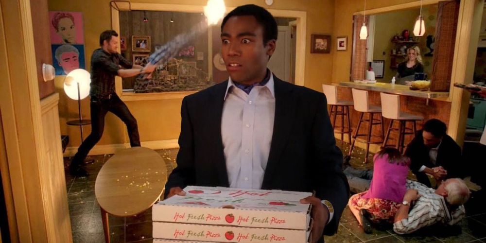 A scene from Community where Troy holds pizza boxes while chaos is happening in the apartment behind him. 