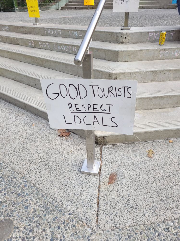 A white sign with black lettering taped to a railing that reads: "GOOD TOURISTS RESPECT LOCALS"