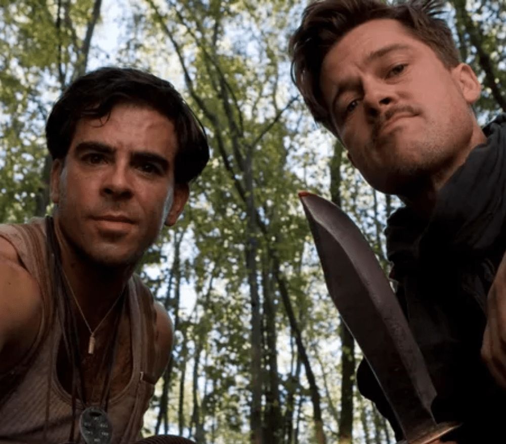 Two men, the characters "The Bear Jew" and Lt. Aldo Raine looking down at the camera which is from the POV of a nazi soldier. Aldo is holding a large knife which is about to be used to carve a swastika on the Nazi's forehead so he can never hide who he is.