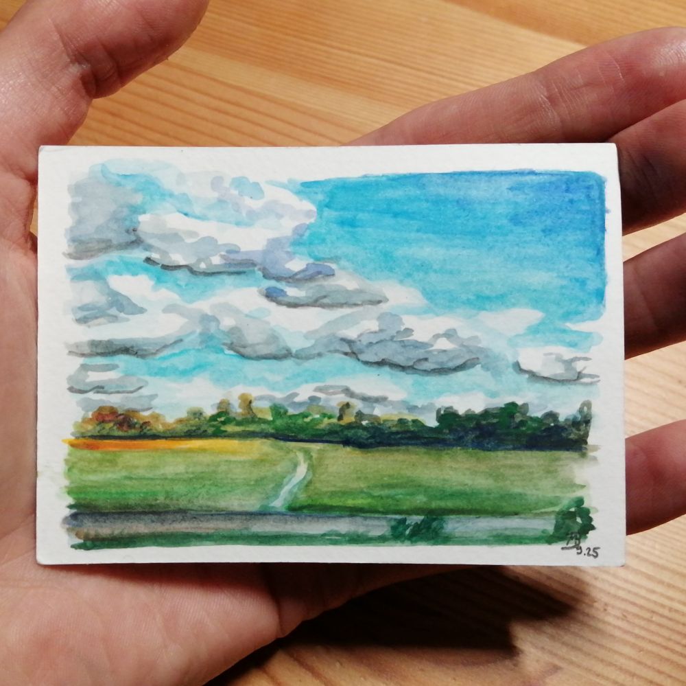 In der Hand gehaltene kleine Aquarell-Skizze. Sie zeigt eine einfache Weidelandschaft mit Bäumen am Horizont. Der Großteil des Bildes wird von blauem Himmel mit größeren Schönwetterwolken
