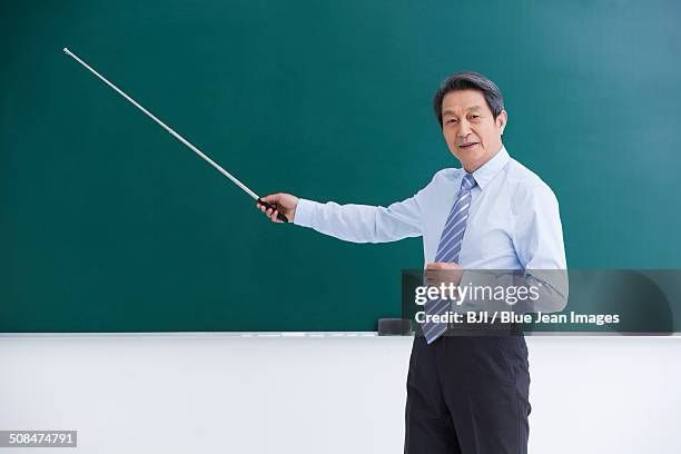 getty image of a sharply dressed man, possibly a professor using a stick to point at an empty chalk board 