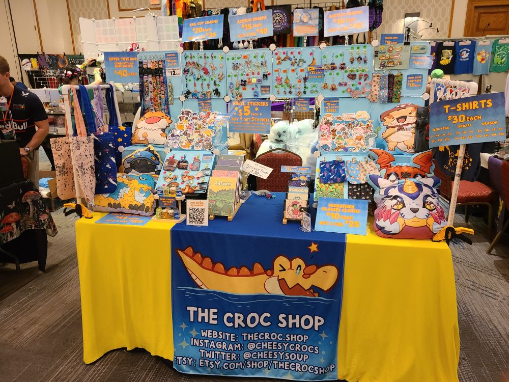 The Croc Shop's yellow and blue table filled with all kinds of bright and colorful creature merchandise. 