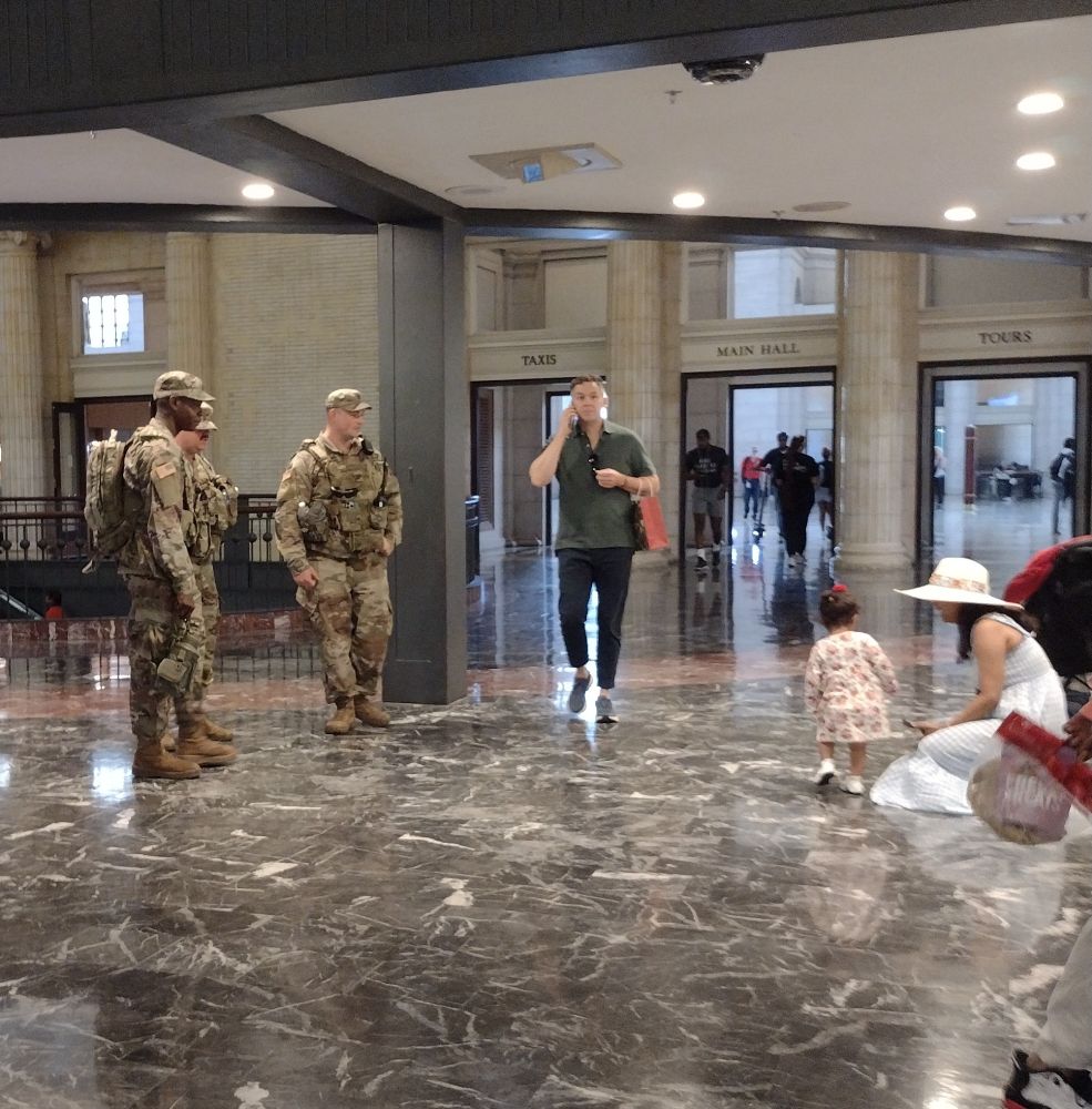 Three soldiers so bored that small child looking at them with her mother looks like their only break in monotony for the day, plus one guy walking through with a purpose, on his cell, because absolutely nothing other than transportation is happening in the transportation hub. Mom's back is to Neuhaus, the fancy chocolatier. The door to Blue Bottle Coffee is visible behind the soldiers.