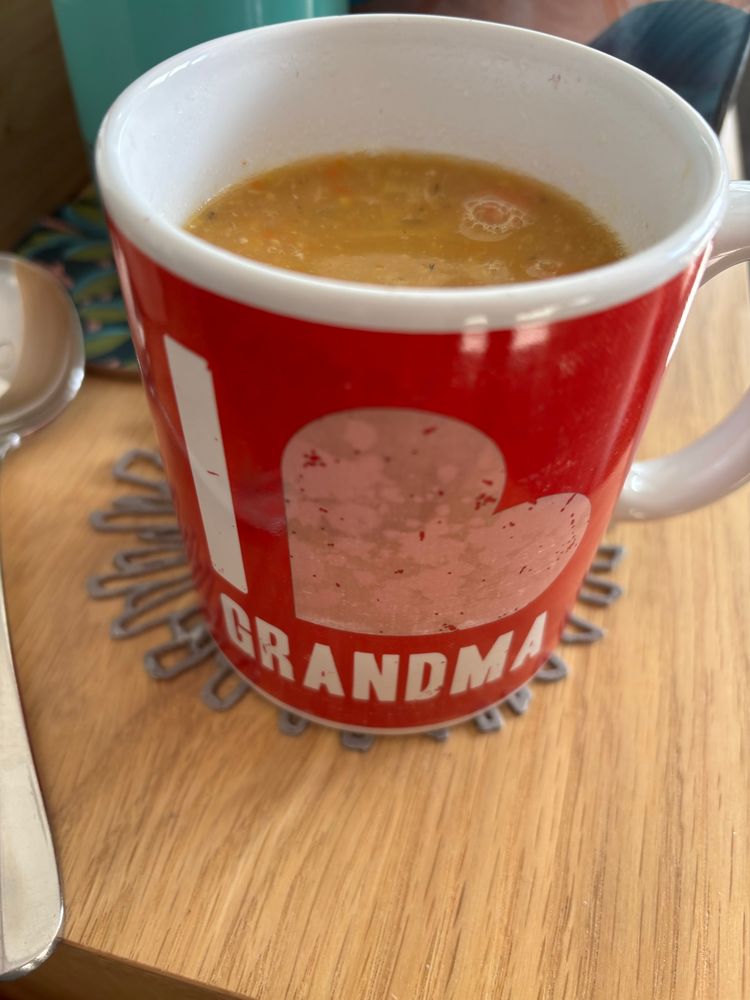 A red and pink cup with I 🩷 Grandma on it and piping hot vege soup inside. 