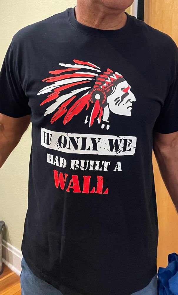 A tshirt with a full-headdress Indigenous head and under it “If only we had built a wall”