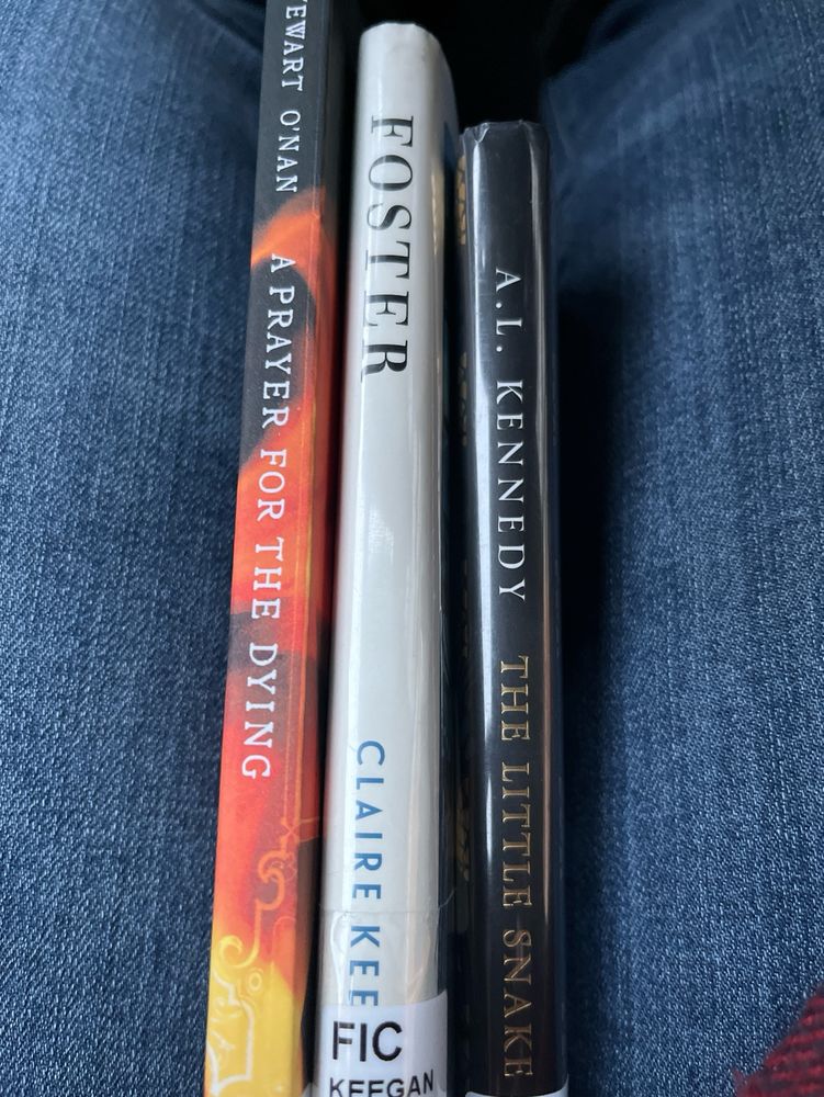 Book spines of Stewart O’Nan’s “A Prayer For The Dying,” Claire Keegan’s “Foster,” and A.I. Kennedy’s “The Little Snake” are sandwiched between denim. 