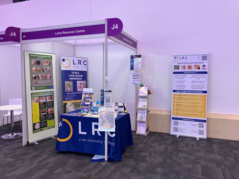 Conference stand ready for action with banners, leaflets and a blue table cloth with the Lyme Resource Centre logo in blue white and yellow. Banner reads - Could it be Lyme disease? TARGET T- tick bites are painless and easily missed A - Aches and pains R - Rash expanding G - Generalised non-specific symptoms E - Every system T - Treat