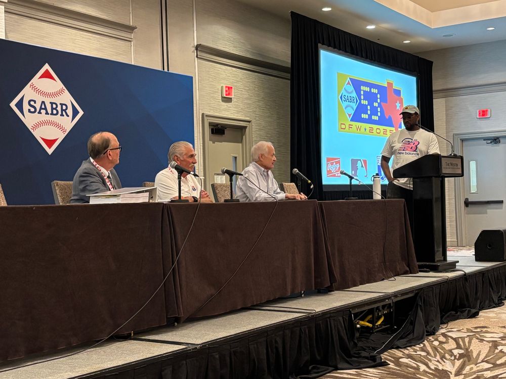 Three panelists seated and moderator at the podium with the SABR logo behind 