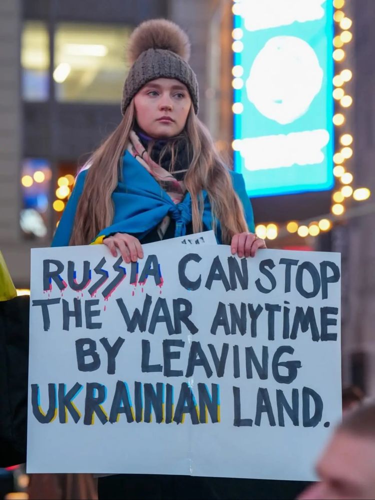 Photo of woman holding a sign that says Russia can stop the war anytime by leaving Ukrainian land 