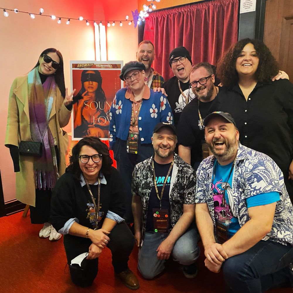 Anomaly crew group photo with Yuka Someya next to the SOUND OF LOVE poster.