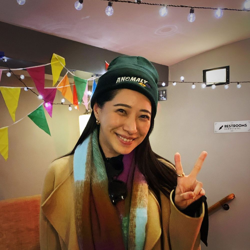 Yuka Someya wearing an Anomaly hat, smiling, and giving the peace sign.