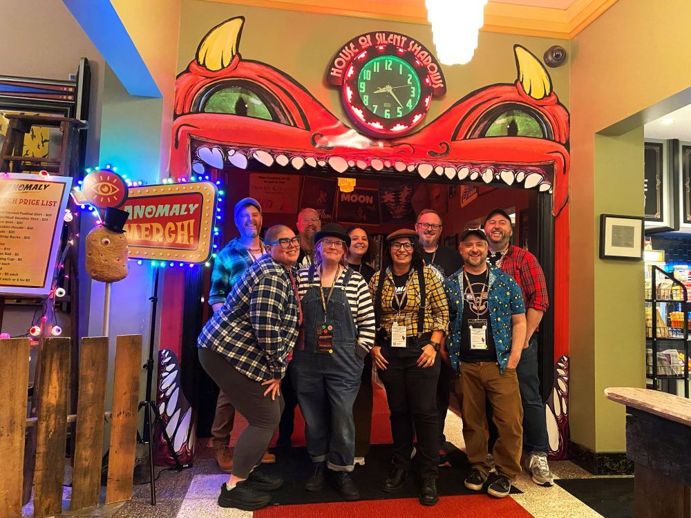 Anomaly crew group photo under a carnival funhouse style devil mouth arch.