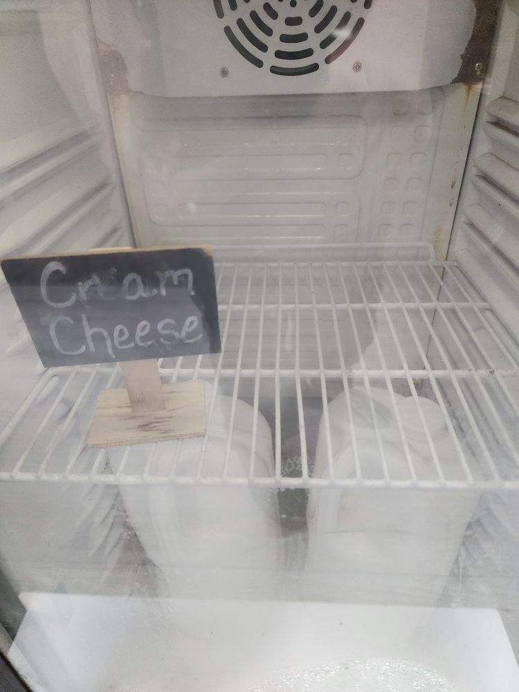 A see-through refrigerator door showing a sign that says cream cheese, but there is no cream cheese.