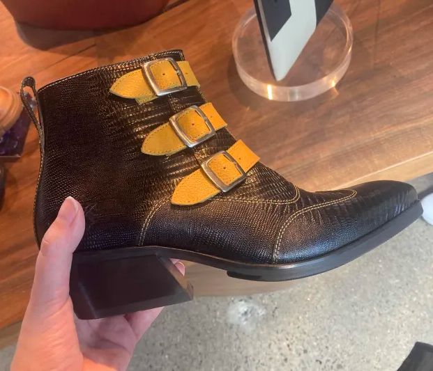 a pointed black ankle boot with snakeskin patterned leather and three yellow buckles