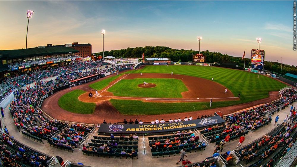 Image shows a view of the field at Ripken Stadium at sunset. A baseball game is being played and the pitcher is at the release point of his pitch.