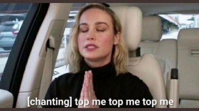 Brie Larson chanting “top me top me top me top me” in the passenger seat of a car with tan interior leather