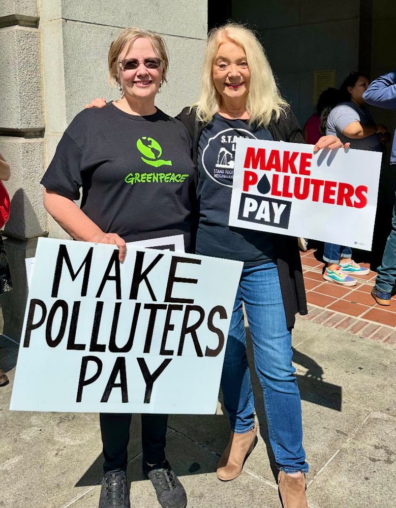 Women in Greenpeace and Stand LA shirts hold MAKE POLLUTERS PAY protest signs in front of L.A. City Hall.