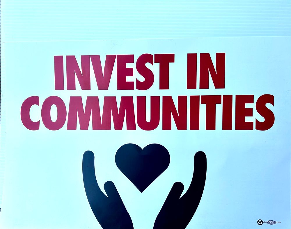 Sign says INVEST IN COMMUNITIES with image of two hands and a heart. 