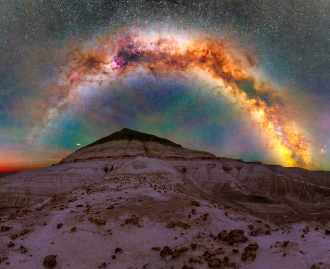 A colorful view of the Milky Way galaxy in the sky over a mountain.