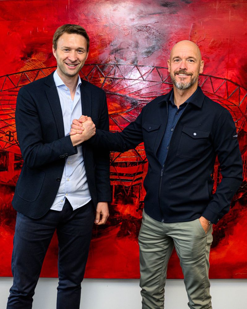 Simon Rolfes & Erik ten Hag schütteln die Hände vor einer roten Wand mit einem Bild der BayArena 