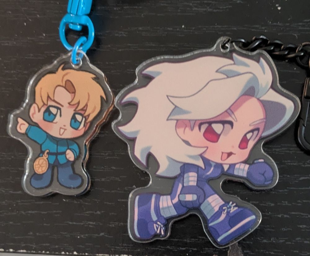 Two acrylic keychains. The one on the left is Rafal from Orb Movements of the Earth. On the right is a Noi from Dorohedoro. 
